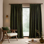 Full-length olive green washed velvet curtains framing a large window in a neutral living room, styled with a wooden armchair, matching green cushion and natural accessories.