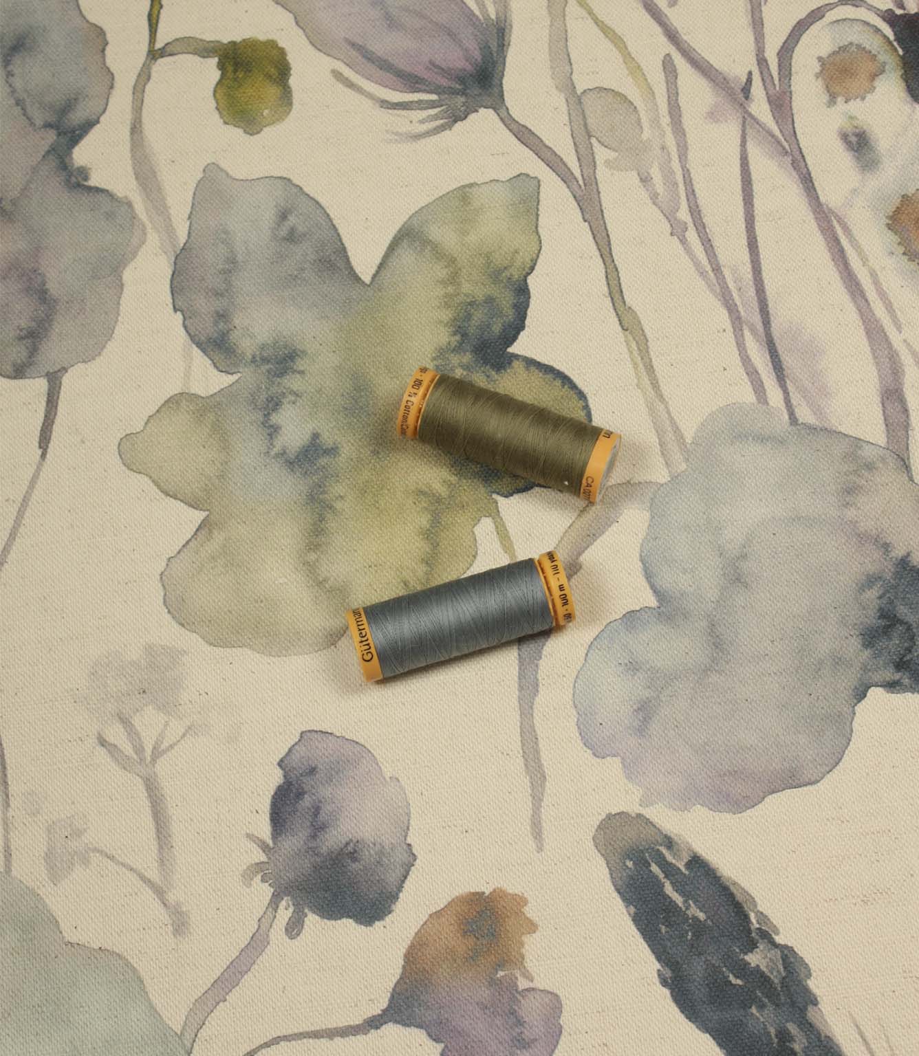Hibberia Crocus cotton fabric with matching thread spools, highlighting the floral pattern in soft blue, green and lilac tones.