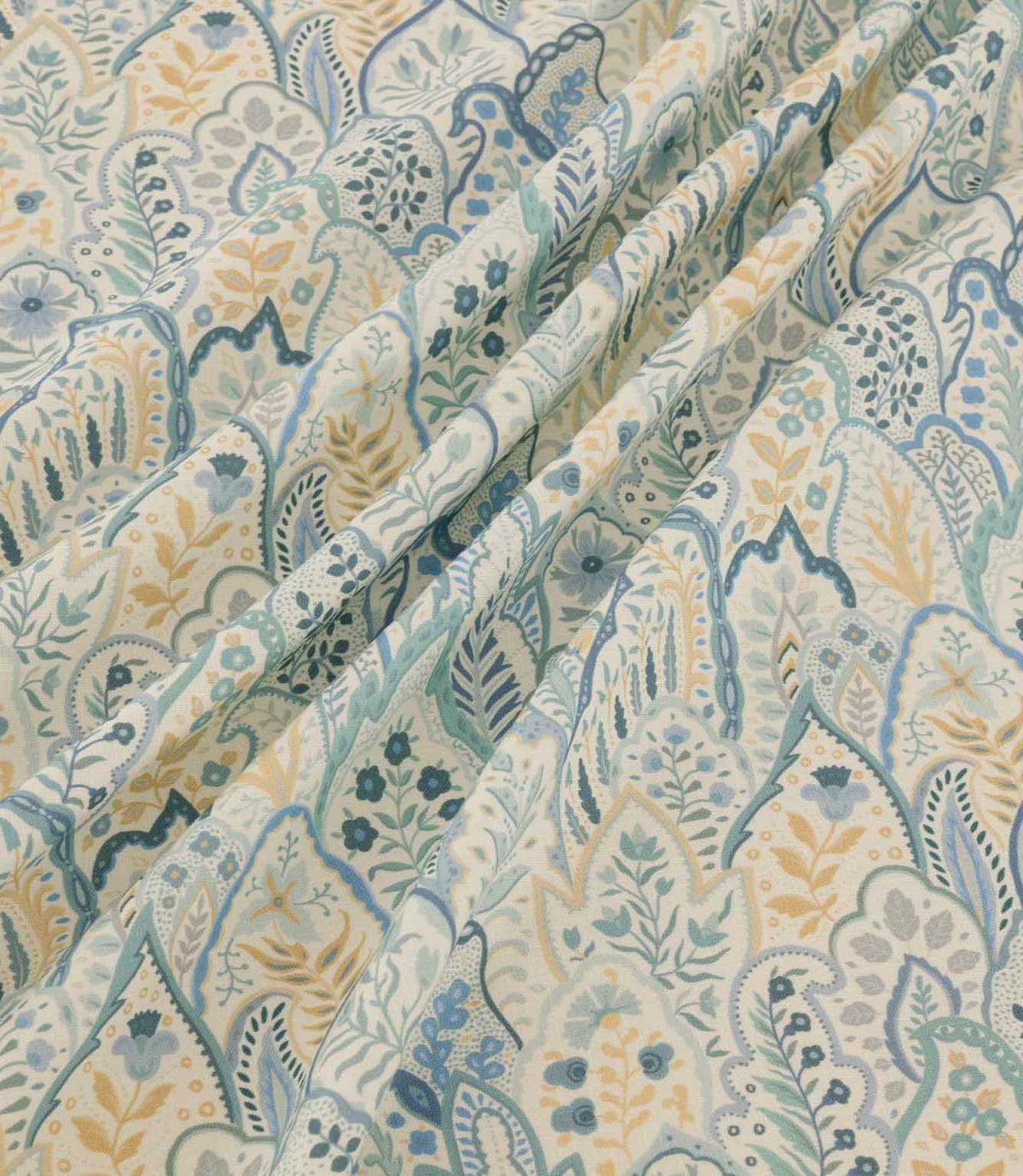 Hitherhill Saltwater floral fabric arranged in soft, flowing folds, showcasing its detailed botanical pattern of layered leaves, delicate flowers and decorative foliage in aqua, muted teal, blue and pale yellow on an ivory background.
