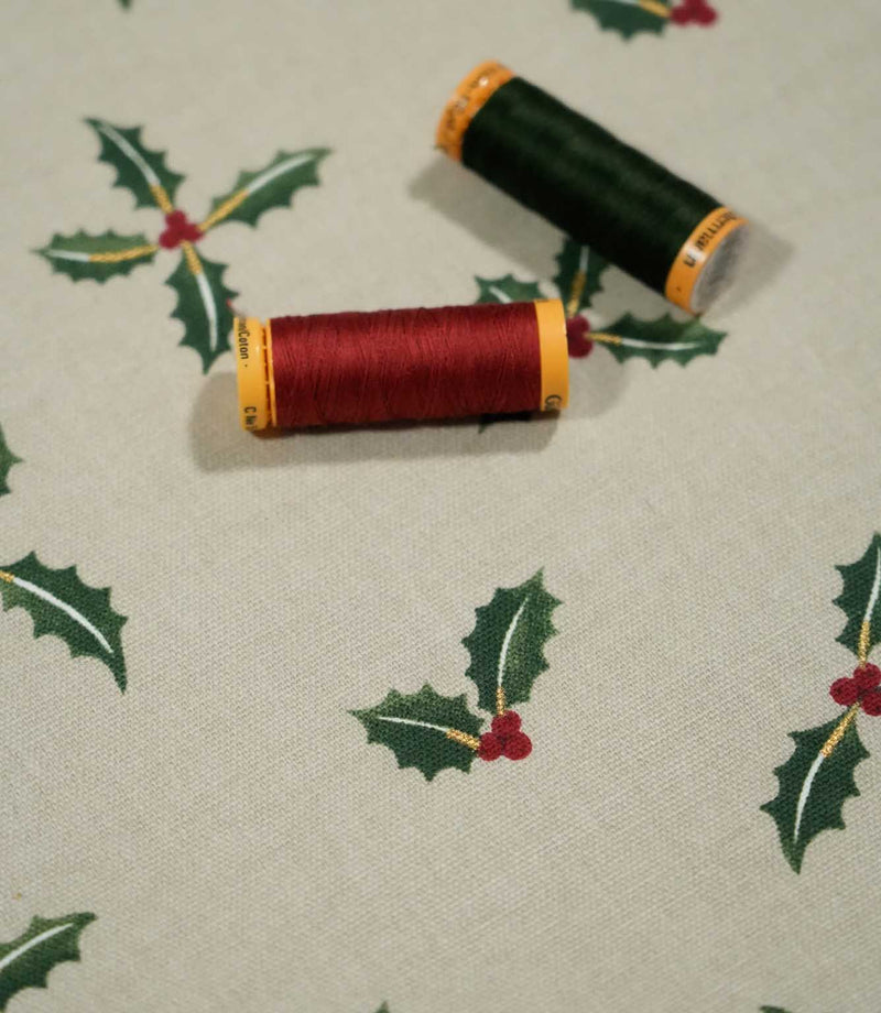 Holly and Berry Stone Christmas fabric with coordinating red and green thread spools, highlighting the festive holly leaf and berry pattern on a stone background.