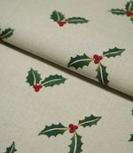 Folded Holly and Berry Stone fabric showing the repeating green holly and red berry design with subtle gold accents across a textured neutral ground.