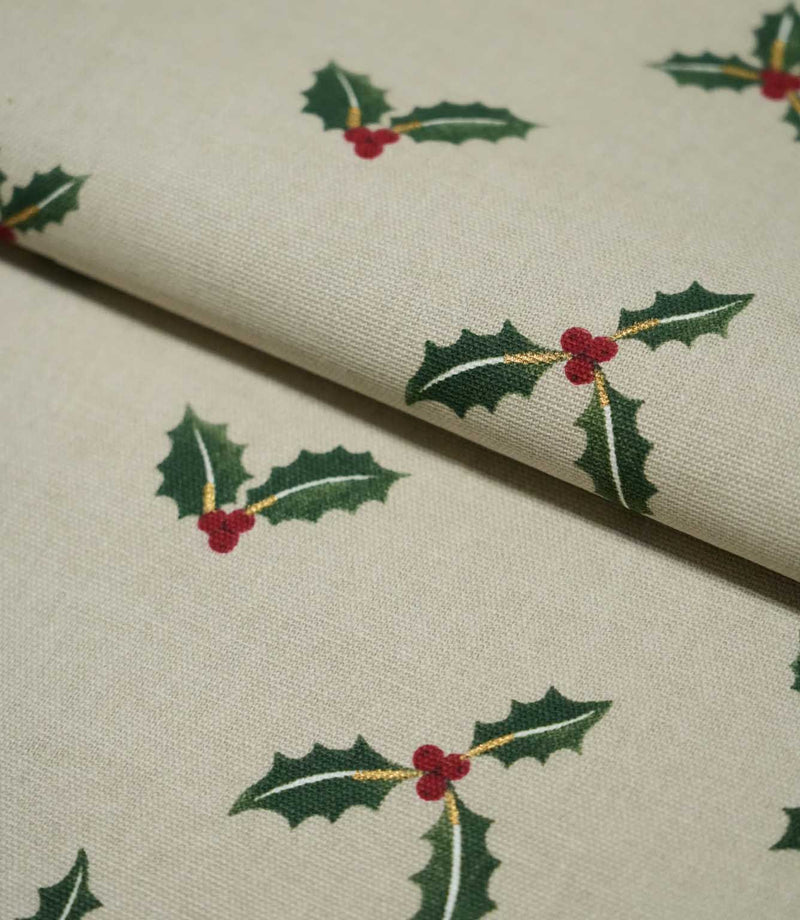 Folded Holly and Berry Stone fabric showing the repeating green holly and red berry design with subtle gold accents across a textured neutral ground.