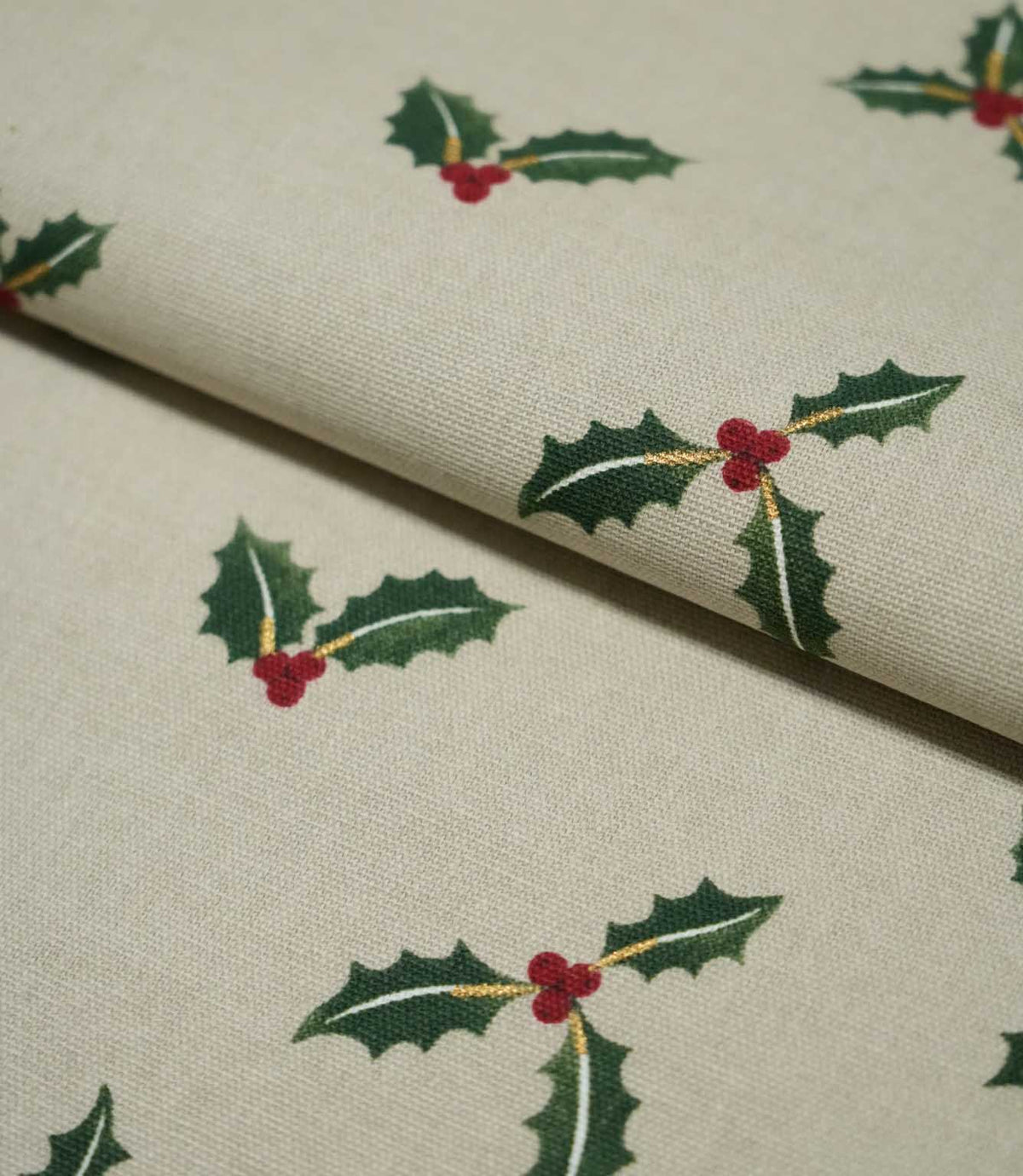 Folded Holly and Berry Stone fabric showing the repeating green holly and red berry design with subtle gold accents across a textured neutral ground.