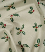 Draped Holly and Berry Stone Christmas fabric displaying its woven texture and scattered festive pattern of green holly leaves, red berries and gold detailing.