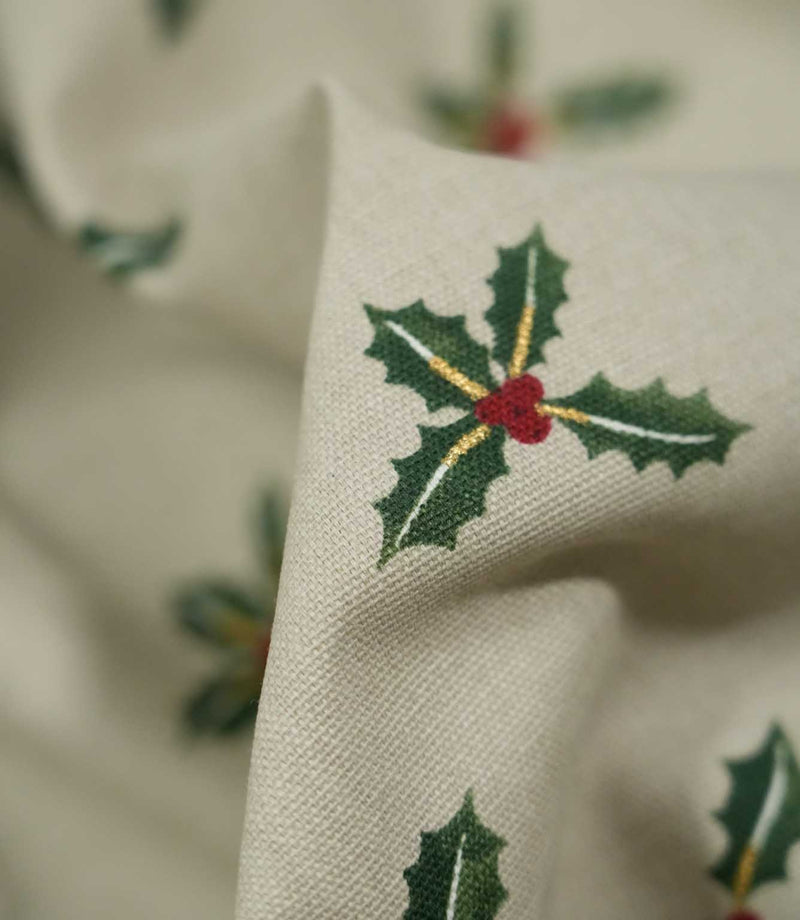Detailed close-up of Holly and Berry Stone fabric showing a green holly sprig with red berries and delicate gold accents on a textured stone neutral background.