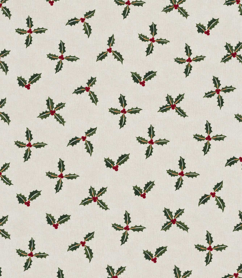 Festive fabric with repeating pattern of green holly leaves with small red berries on a warm off-white background.