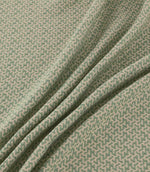 Horton Cascade sage green and natural geometric fabric arranged in soft diagonal folds, showing its textured surface and repeating woven pattern.