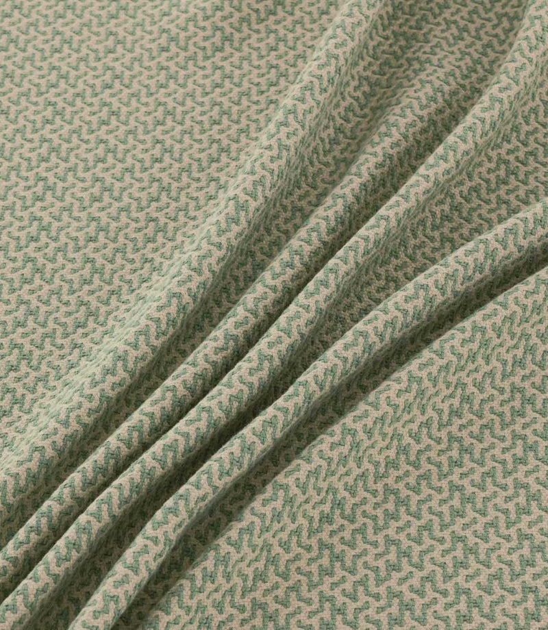 Horton Cascade sage green and natural geometric fabric arranged in soft diagonal folds, showing its textured surface and repeating woven pattern.