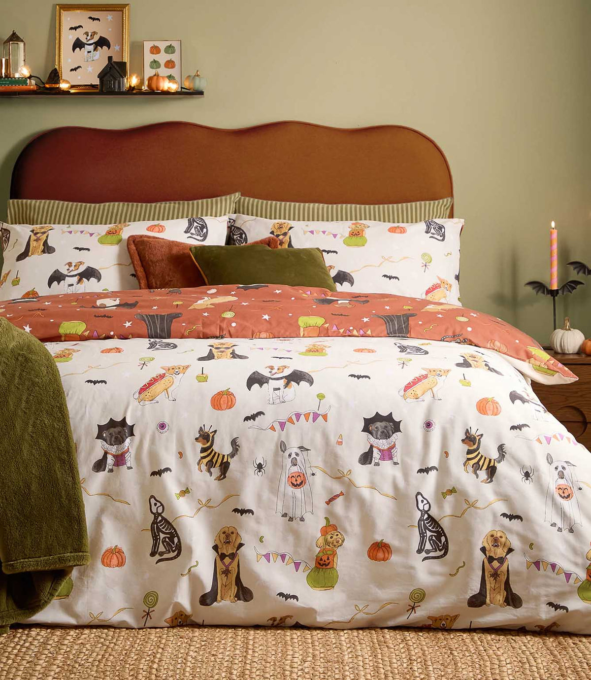 Howl-O-Ween multicolour reversible duvet cover set with illustrated dogs in Halloween costumes, orange pumpkins and black bats on a cream background, styled with rust and olive green cushions.