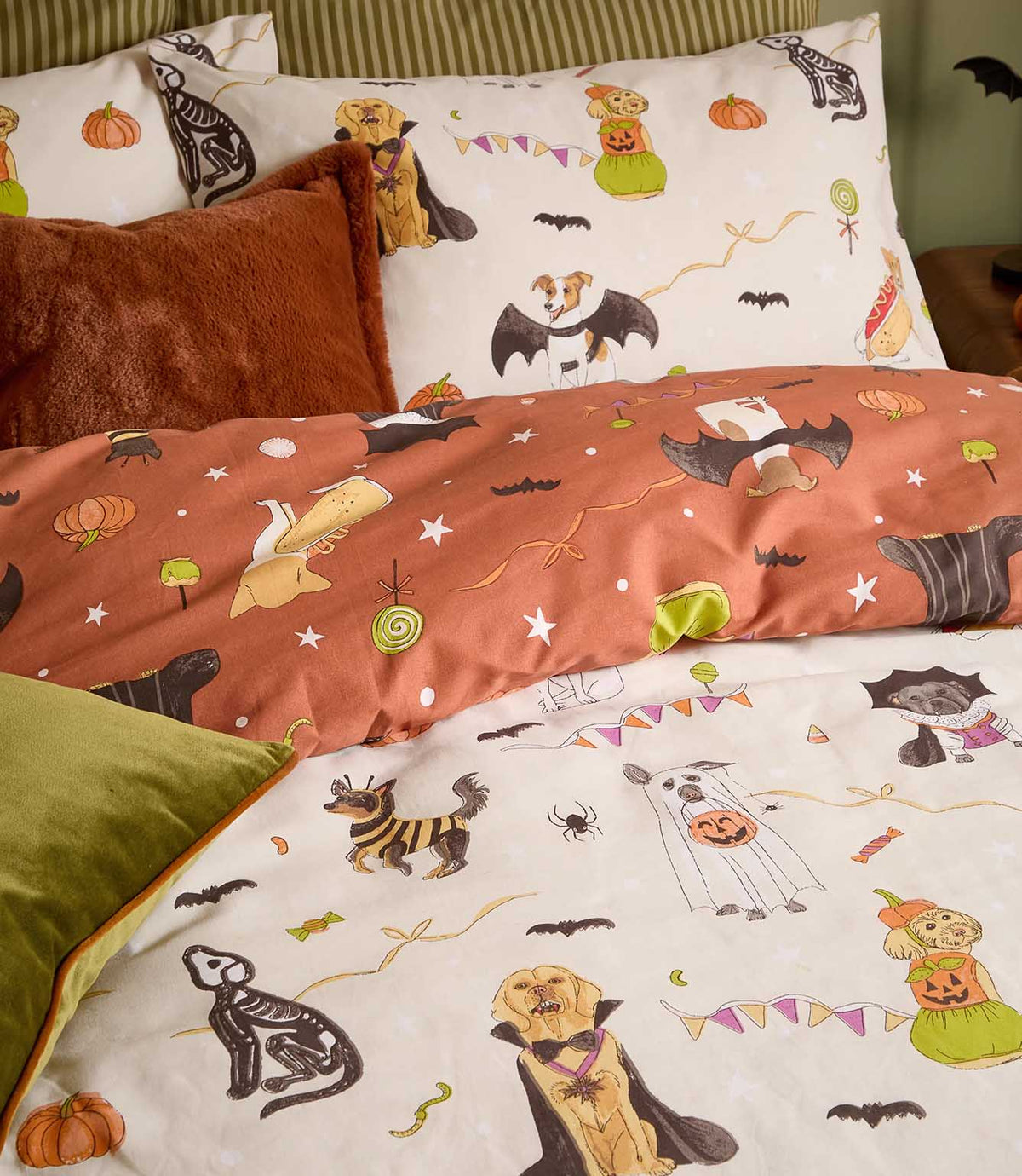 Close-up of the Howl-O-Ween multicolour bedding showing dogs dressed as ghosts, vampires, skeletons and bats, with orange pumpkins and sweets on cream and terracotta backgrounds.