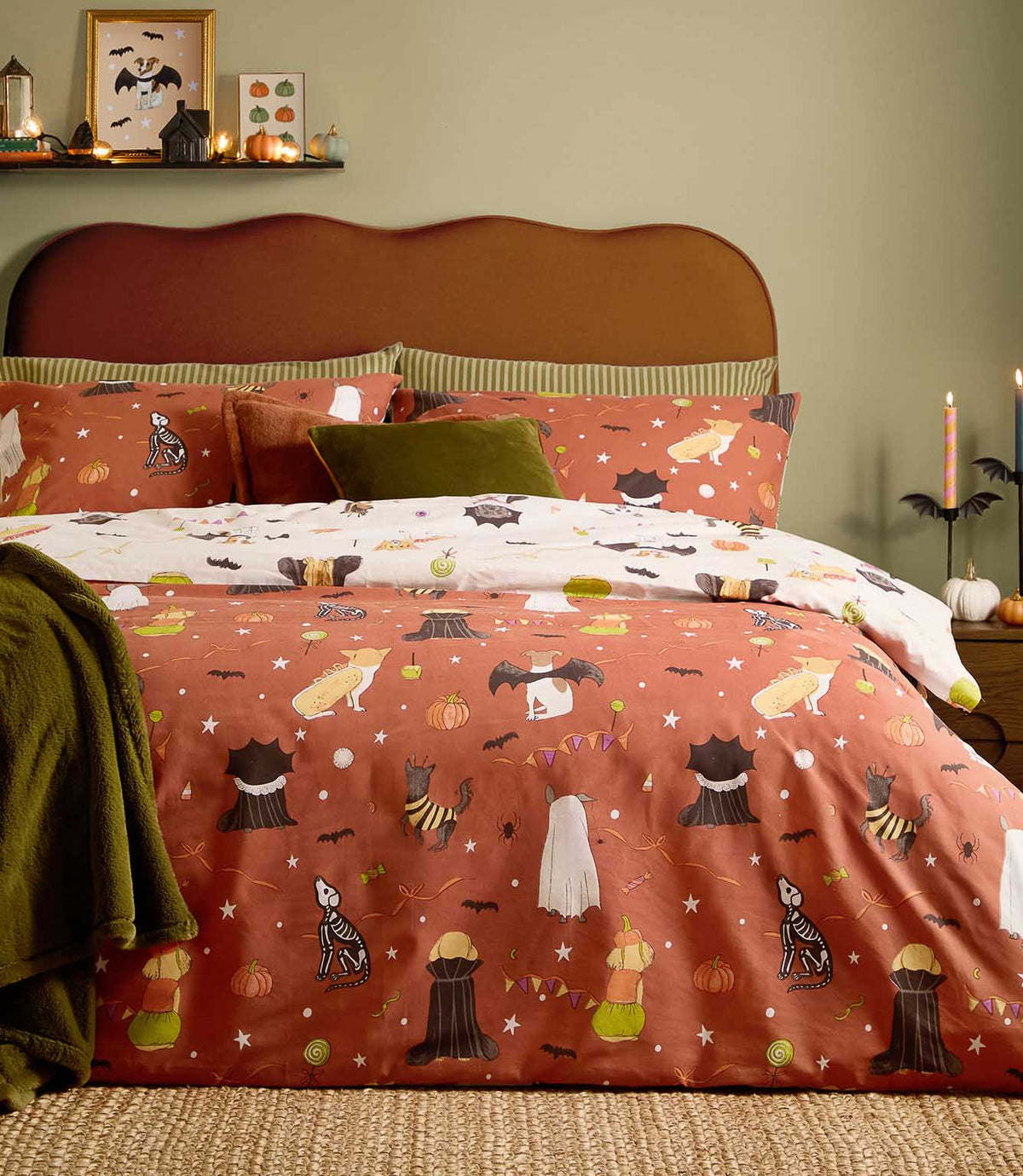 Howl-O-Ween reversible duvet cover shown on its terracotta side with multicoloured costumed dogs, pumpkins, bats and sweets, with the cream printed reverse folded back across the bed.