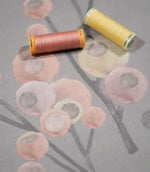 Ichiyo floral fabric laid flat with pink and yellow sewing thread spools, highlighting the soft grey background and delicate pastel botanical print.