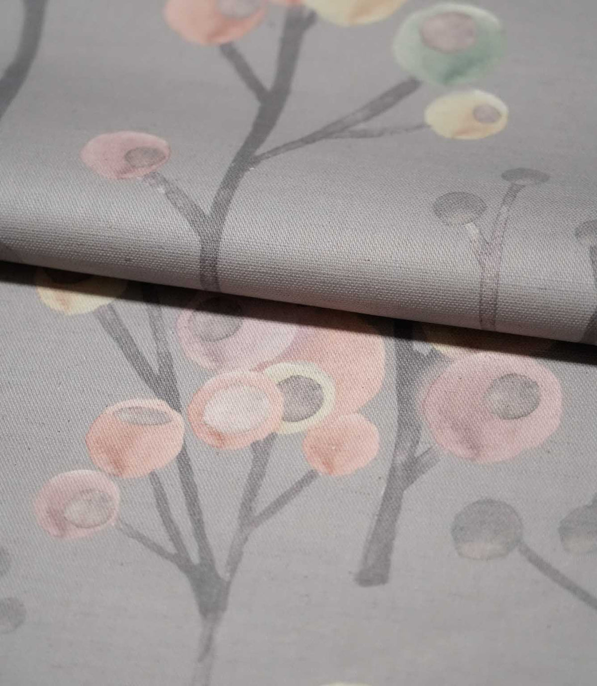 Ichiyo contemporary botanical fabric folded over itself, showing its smooth woven texture and repeating pink, cream and pale green floral design on grey.