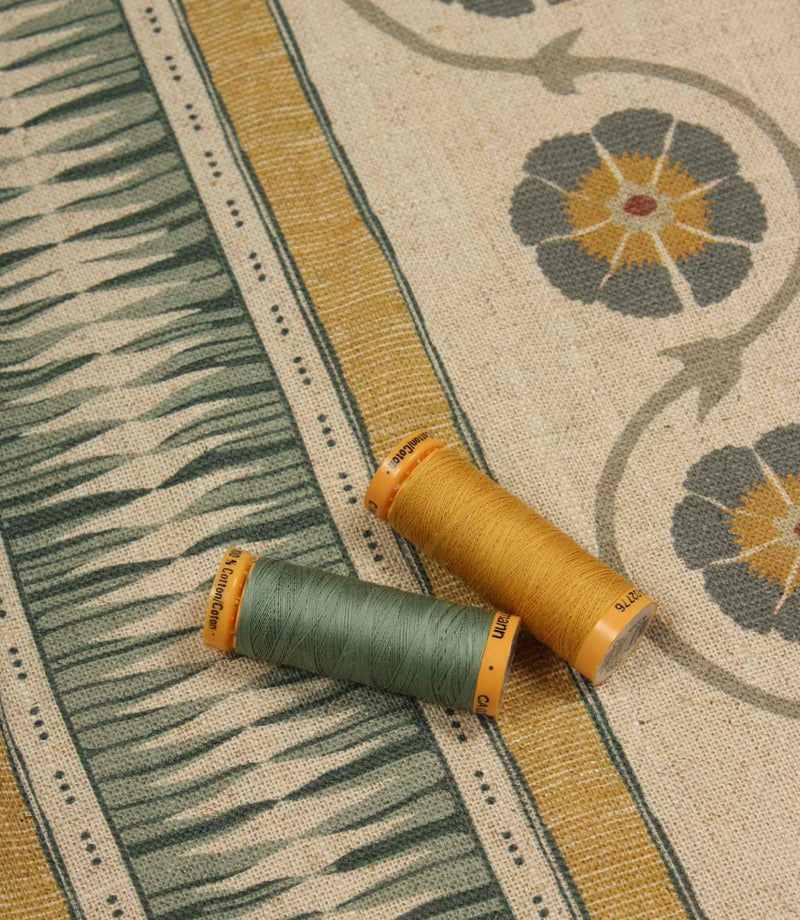 Coordinating thread spools placed on patterned stripe fabric in ochre, sage green, and soft charcoal tones.