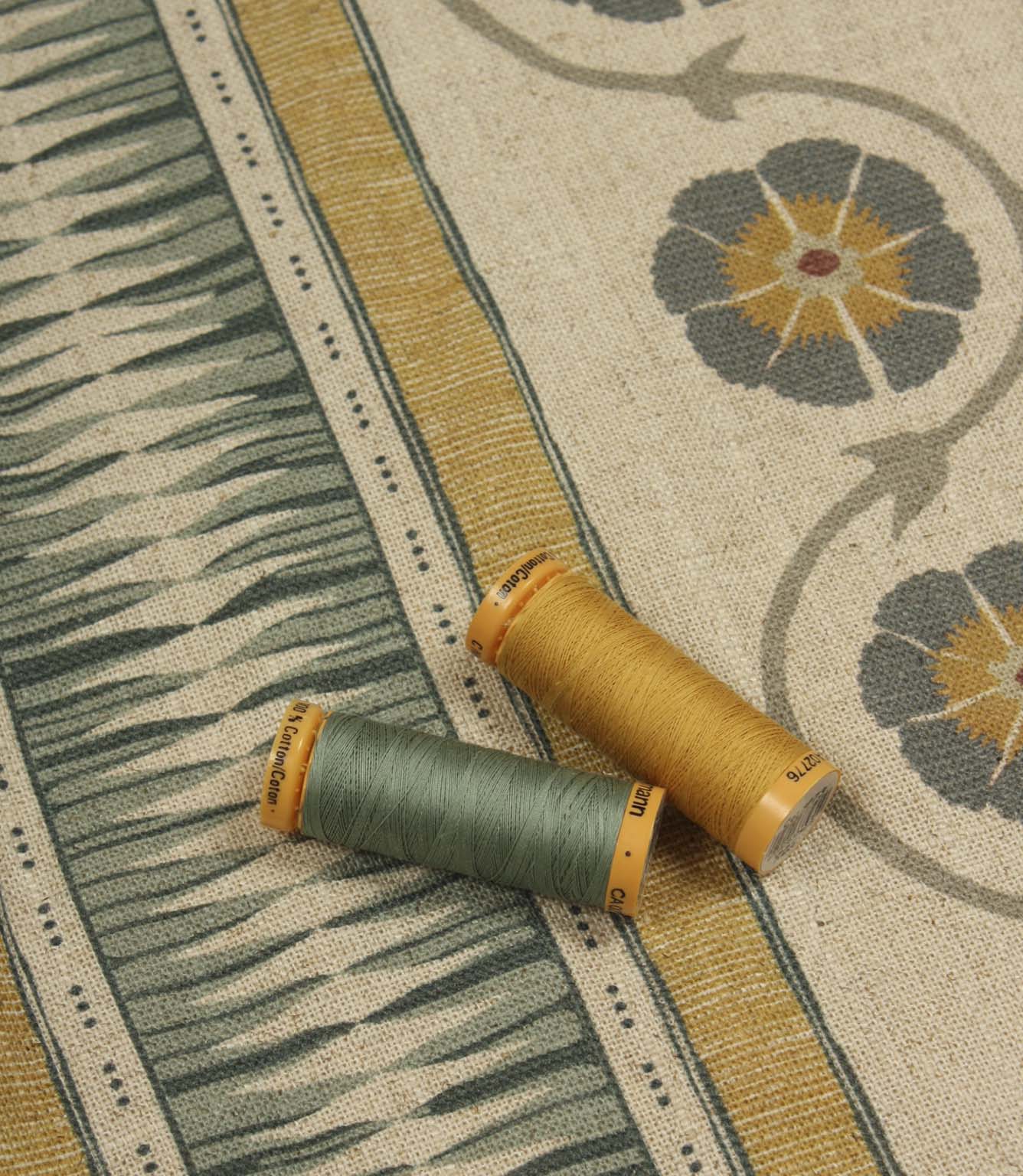Coordinating thread spools placed on patterned stripe fabric in ochre, sage green, and soft charcoal tones.
