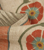Close-up of textured fabric showing woven-look stripes, curved vine motifs, and bold floral medallions in terracotta and blue.