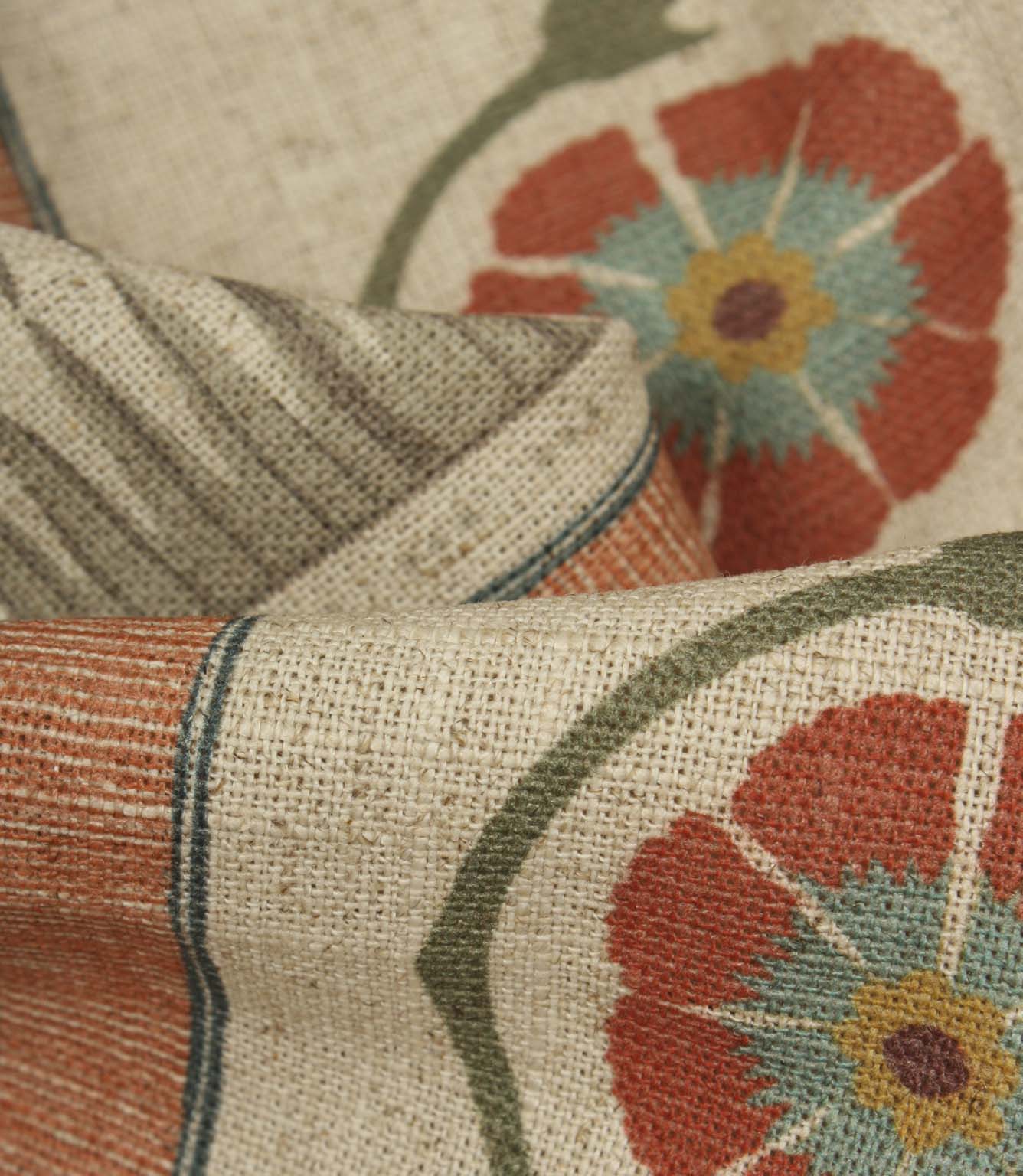 Close-up of textured fabric showing woven-look stripes, curved vine motifs, and bold floral medallions in terracotta and blue.