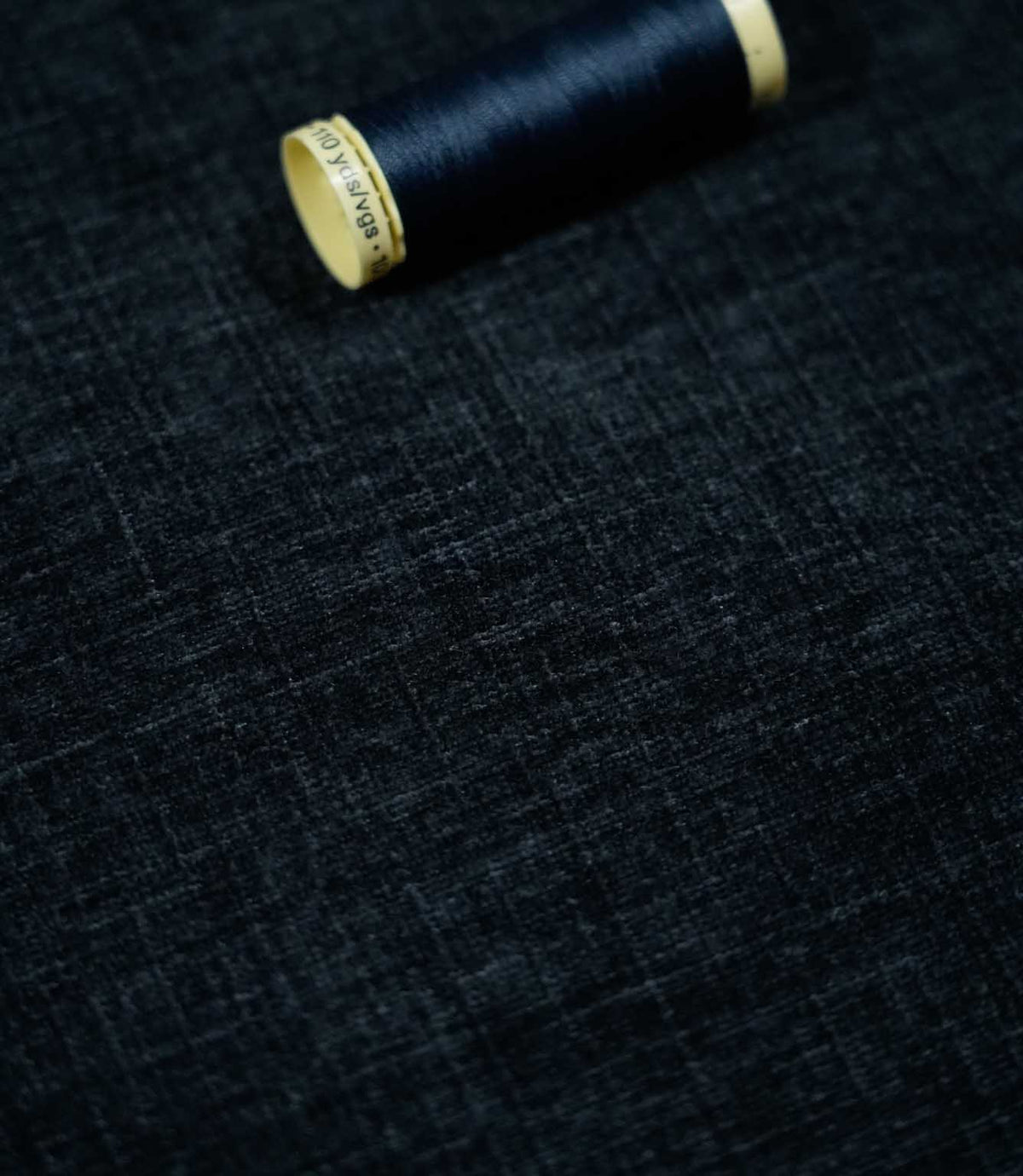 Insernia Velvet Night fabric laid flat with a coordinating dark navy thread spool, highlighting the rich blue-black shade, fine textured appearance and soft velvet finish.