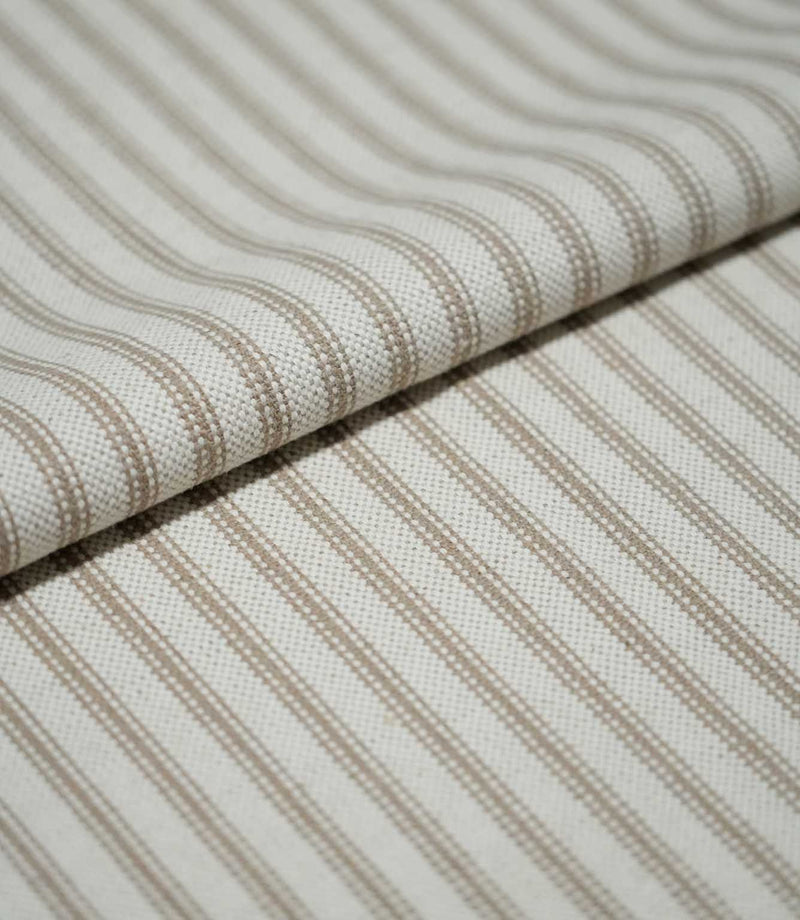 Close-up of folded beige ticking stripe fabric showing the woven texture, natural cream ground and fine neutral striped pattern.