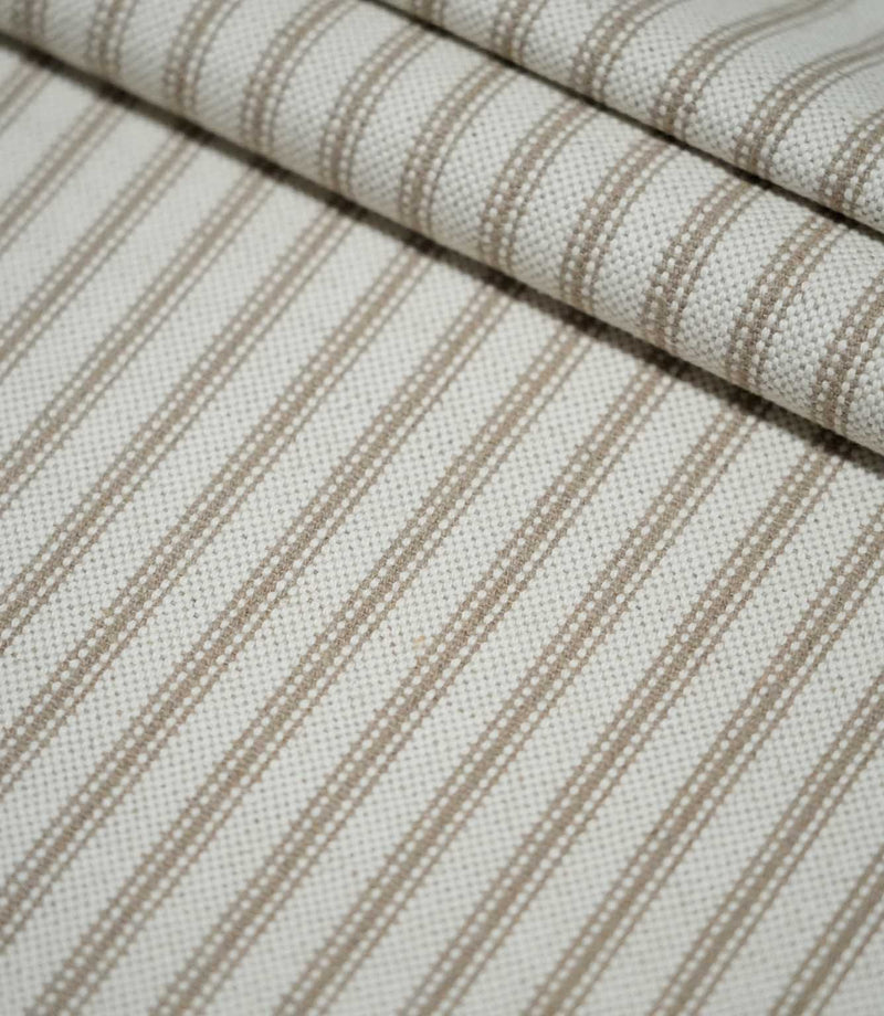 Detailed view of beige ticking stripe fabric arranged in soft folds, highlighting the textured weave and repeating neutral vertical stripe design.