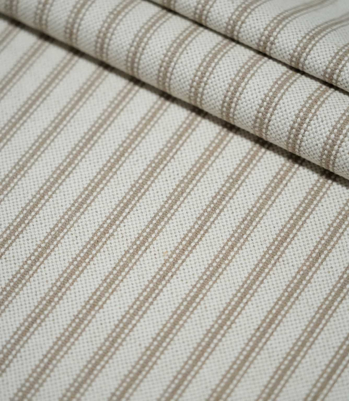 Detailed view of beige ticking stripe fabric arranged in soft folds, highlighting the textured weave and repeating neutral vertical stripe design.