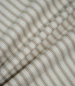Beige ticking stripe fabric draped into soft folds, showing the natural woven texture and evenly spaced taupe-beige striped pattern.