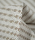 Macro close-up of folded beige ticking stripe fabric, highlighting the tactile woven texture, cream base and detailed taupe-beige stripes.