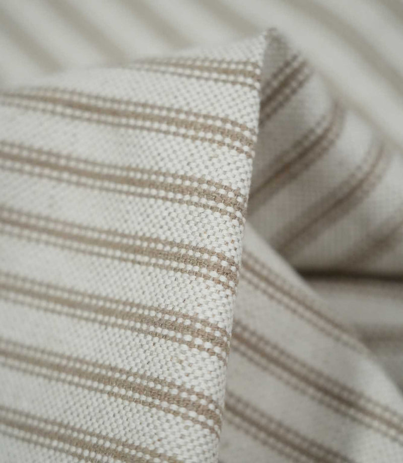 Macro close-up of folded beige ticking stripe fabric, highlighting the tactile woven texture, cream base and detailed taupe-beige stripes.