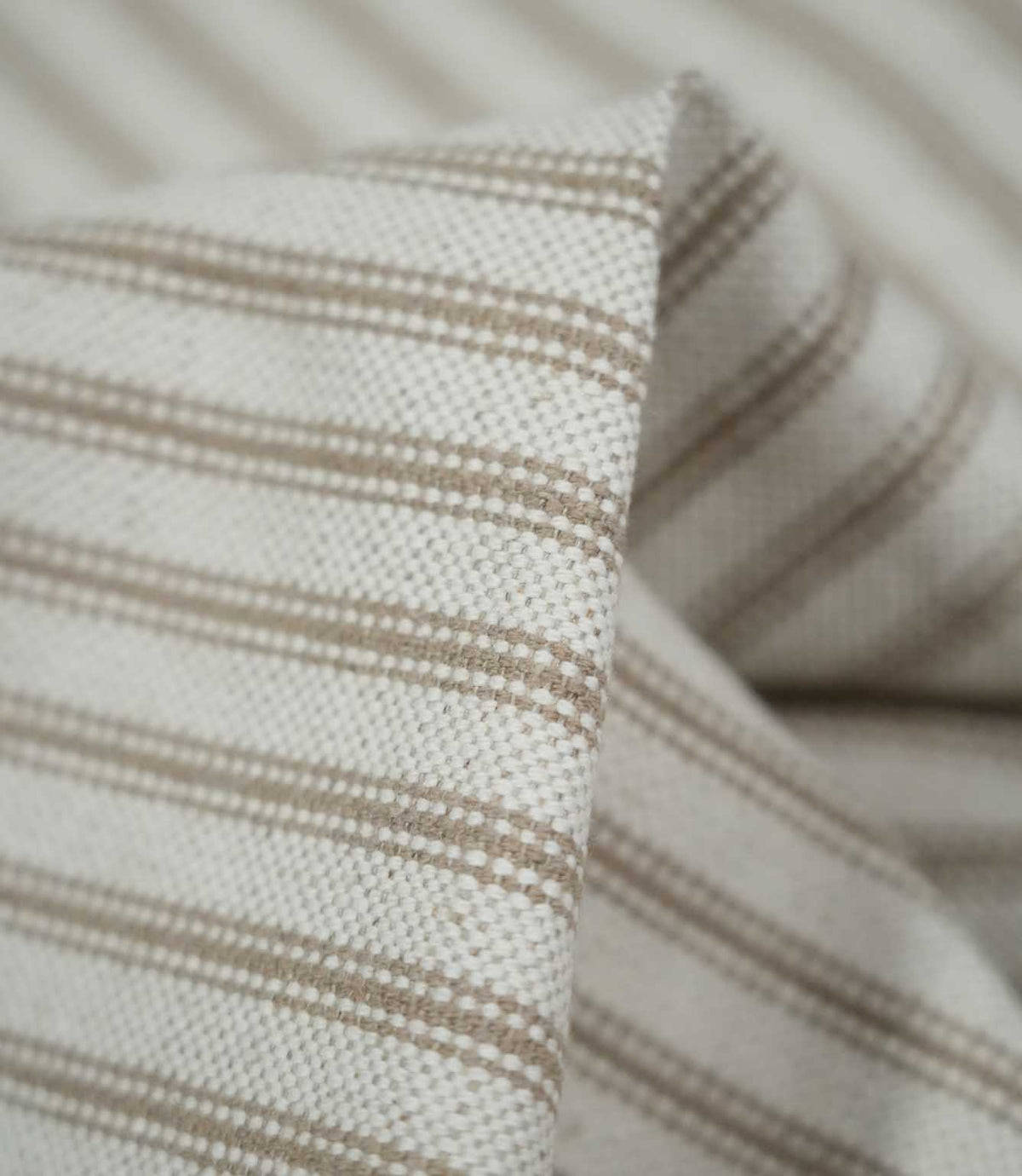 Macro close-up of folded beige ticking stripe fabric, highlighting the tactile woven texture, cream base and detailed taupe-beige stripes.
