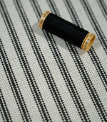 Close-up of black ticking stripe fabric with a black thread spool, highlighting the crisp black stripes and textured natural cream woven ground.