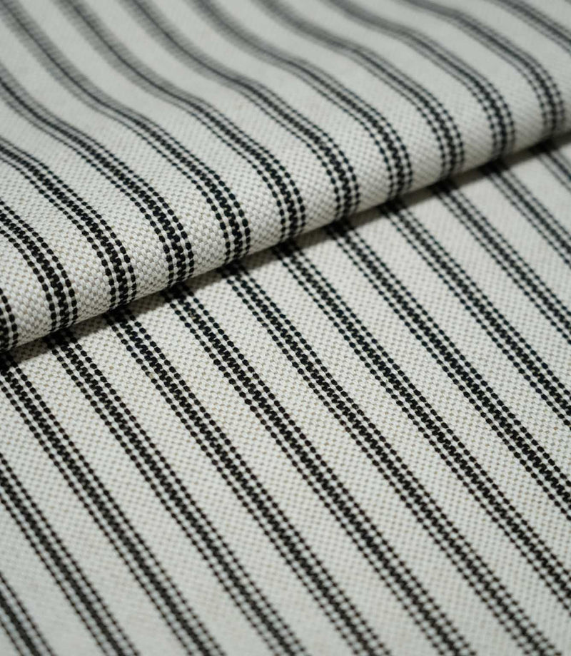 Folded black ticking stripe fabric showing the repeating narrow black stripes, natural cream background and tactile woven texture.
