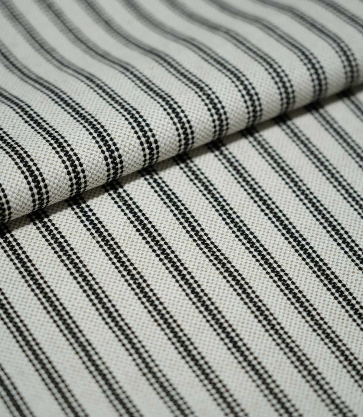 Folded black ticking stripe fabric showing the repeating narrow black stripes, natural cream background and tactile woven texture.