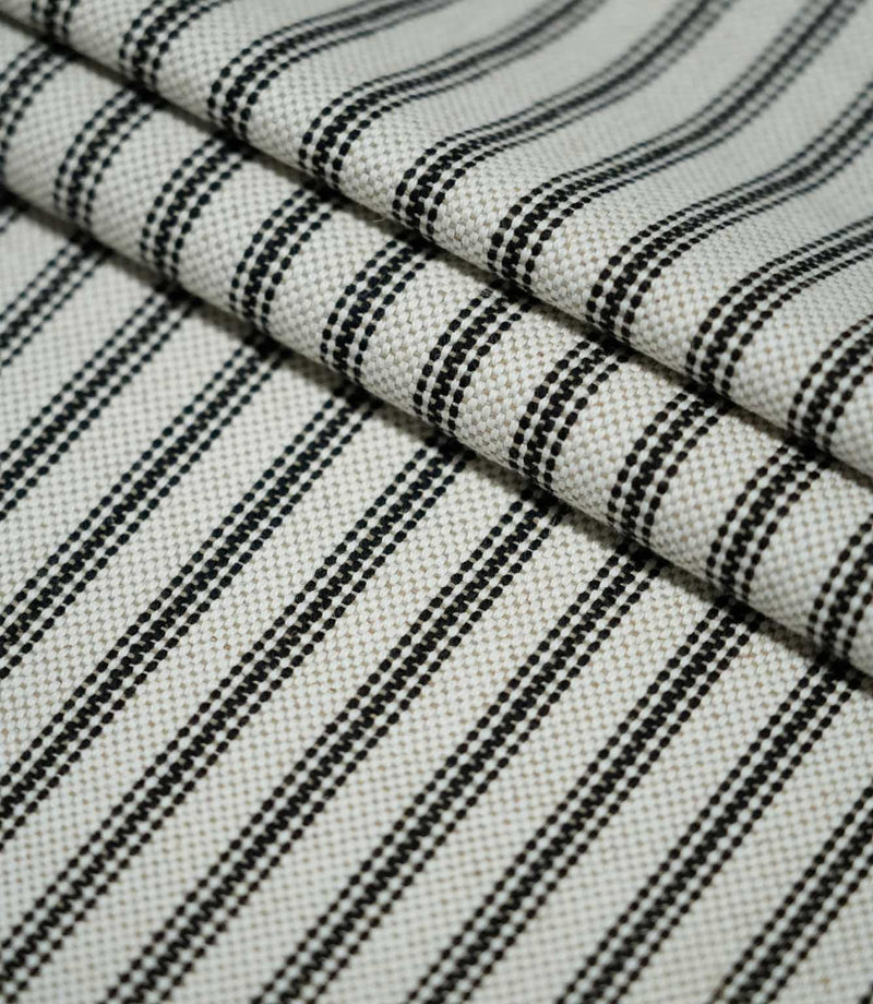 Close-up of layered black ticking stripe fabric, highlighting the structured weave and evenly spaced black stripes against a natural cream ground.