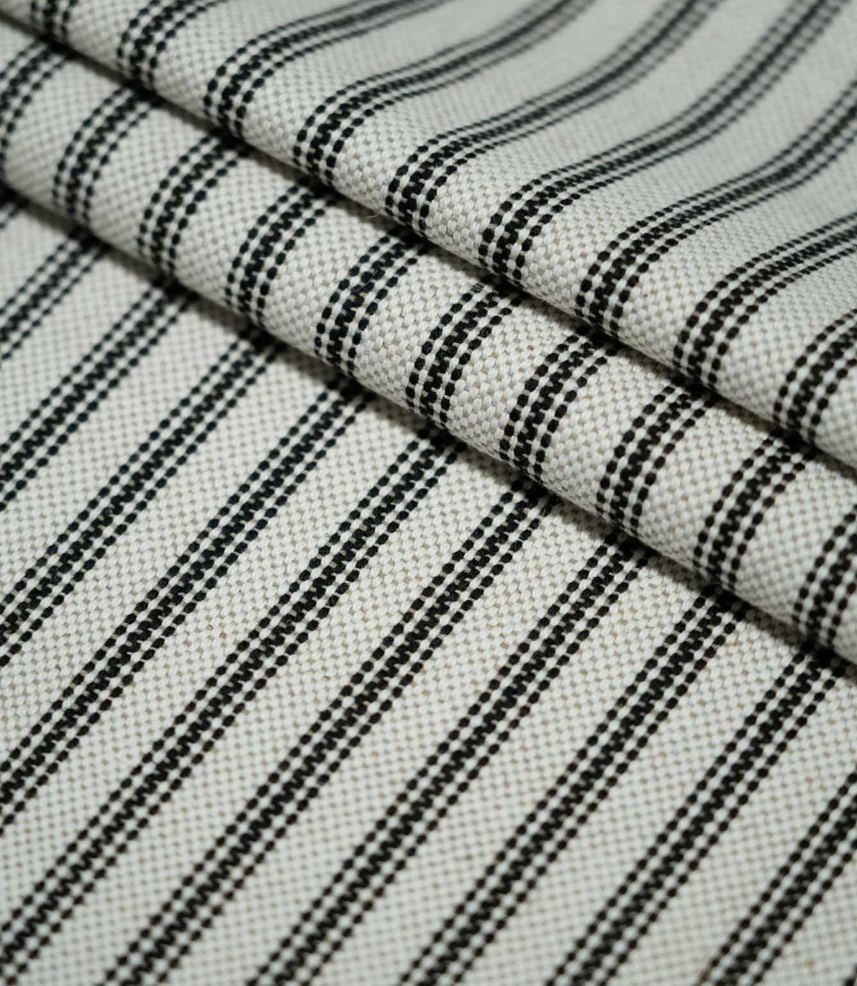 Close-up of layered black ticking stripe fabric, highlighting the structured weave and evenly spaced black stripes against a natural cream ground.