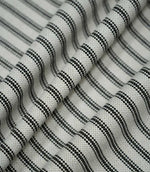 Black ticking stripe fabric arranged in soft folds, showing how the classic black and cream striped pattern drapes while retaining its textured woven finish.