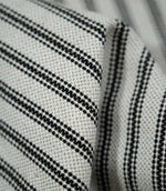 Detailed close-up of folded black ticking stripe fabric showing the natural cream weave and fine black stripes following the soft folds of the material.