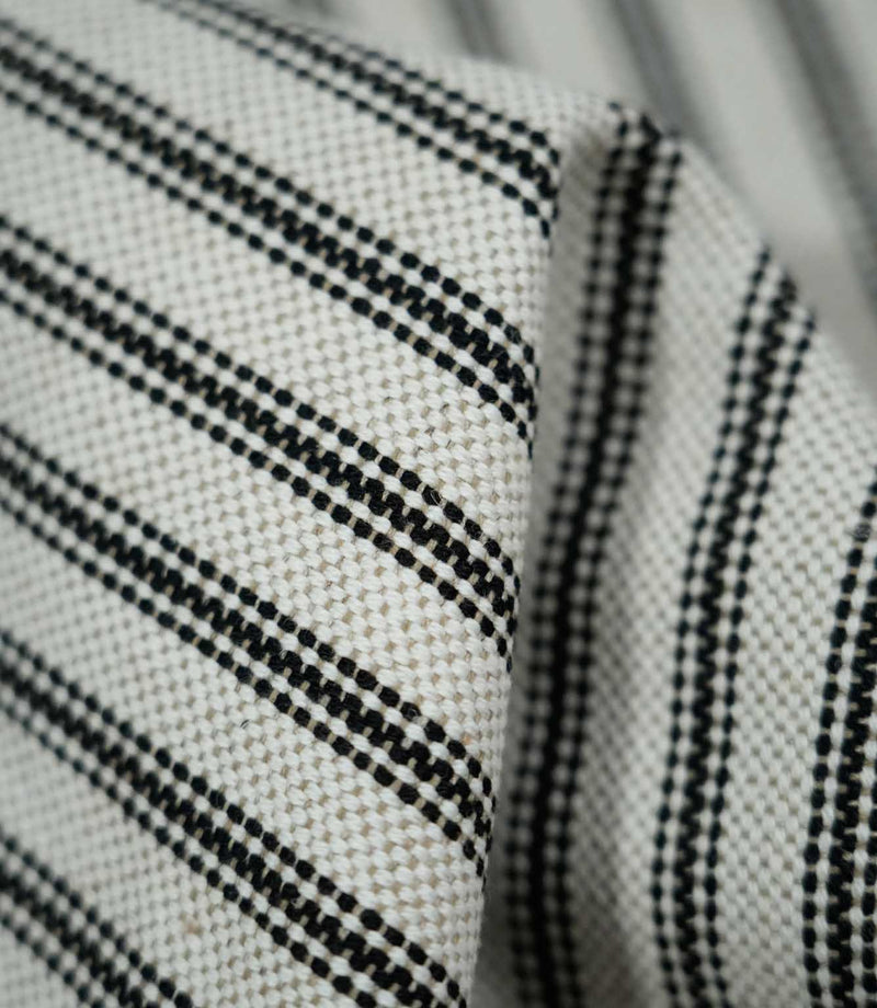 Detailed close-up of folded black ticking stripe fabric showing the natural cream weave and fine black stripes following the soft folds of the material.