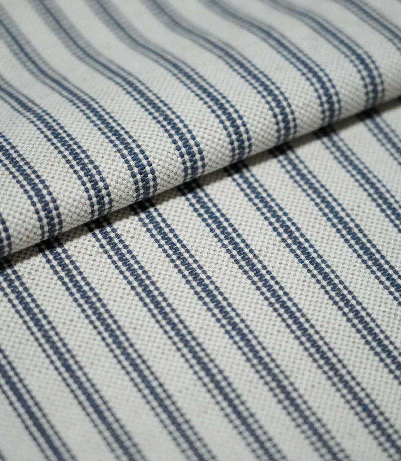 Folded blue ticking stripe fabric showing the repeating navy blue stripe pattern and tactile natural cream woven texture.