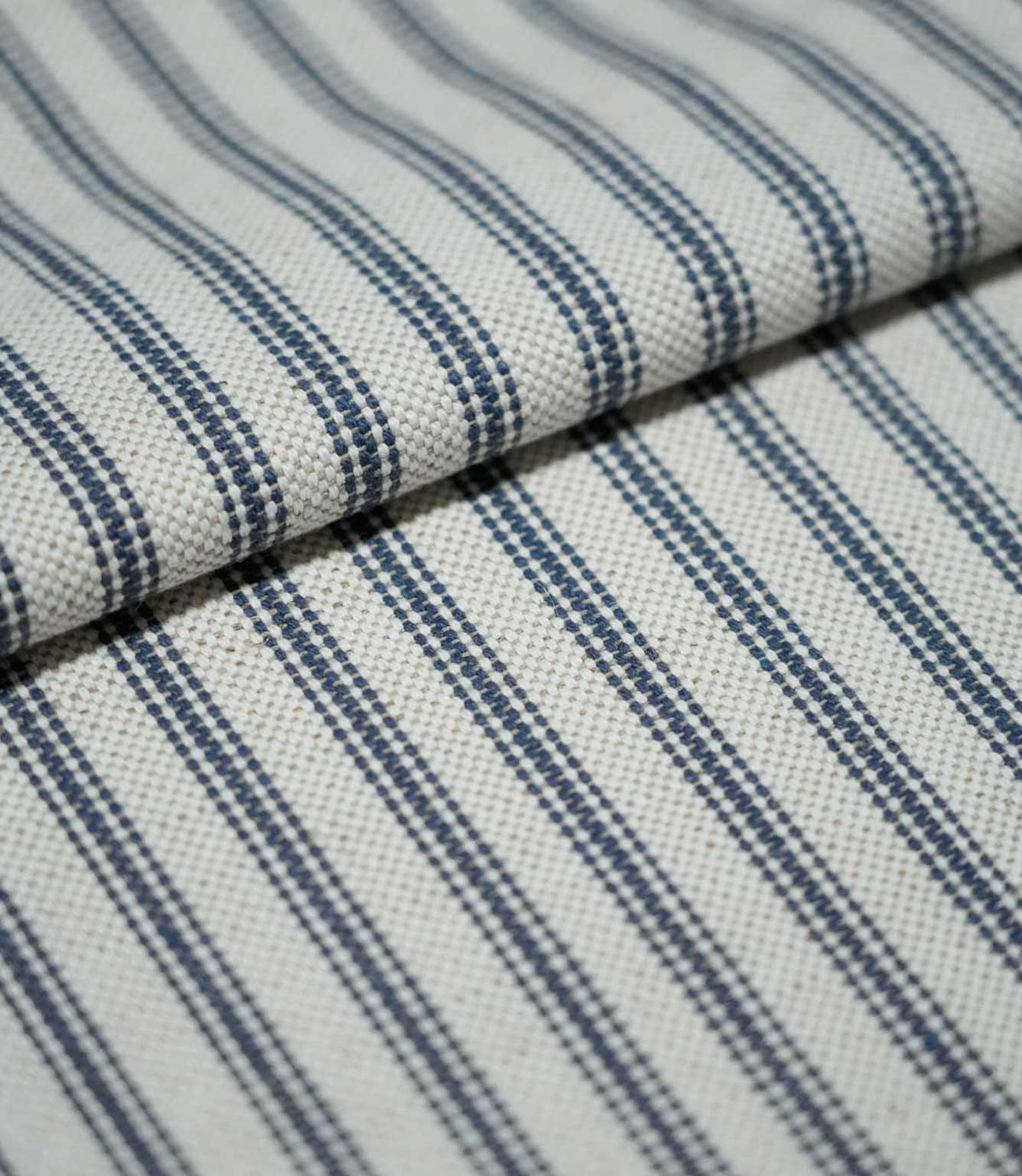 Folded blue ticking stripe fabric showing the repeating navy blue stripe pattern and tactile natural cream woven texture.