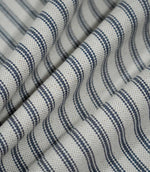 Blue ticking stripe fabric arranged in soft folds, showing the navy striped design following the drape and the textured natural cream weave.