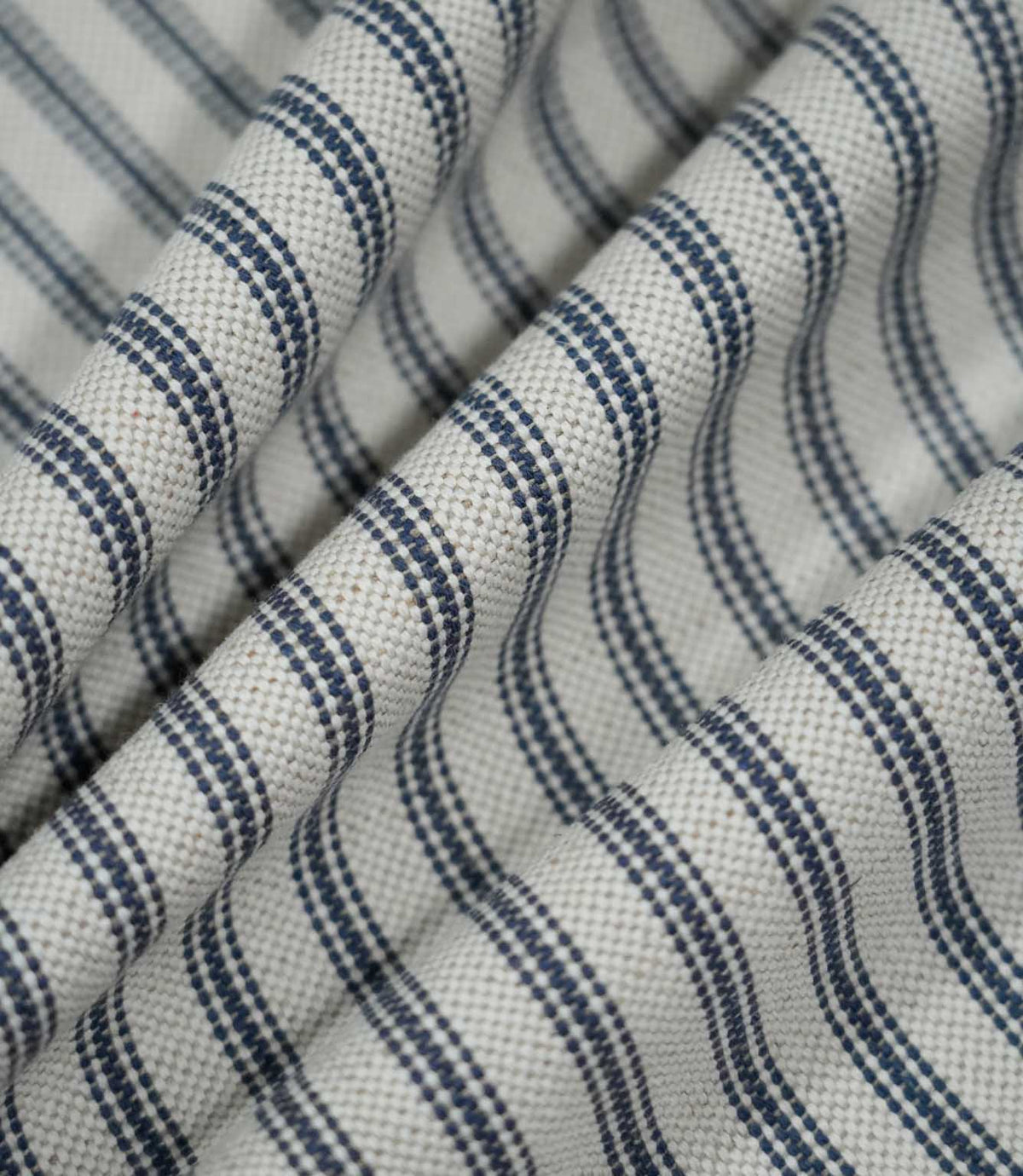 Blue ticking stripe fabric arranged in soft folds, showing the navy striped design following the drape and the textured natural cream weave.