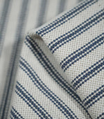 Detailed close-up of folded blue ticking stripe fabric, highlighting the navy blue woven stripes, natural cream background and textured finish.