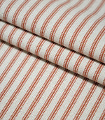 Layers of folded Linen Ticking Burnt Orange fabric showcasing the narrow burnt orange stripes and textured cream woven surface.