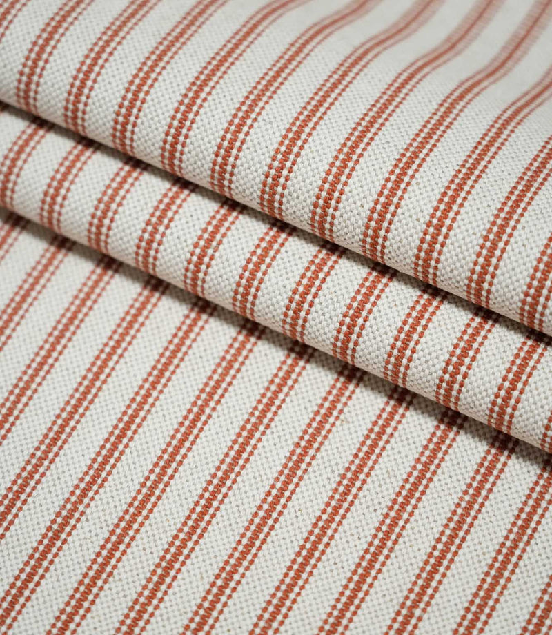 Layers of folded Linen Ticking Burnt Orange fabric showcasing the narrow burnt orange stripes and textured cream woven surface.