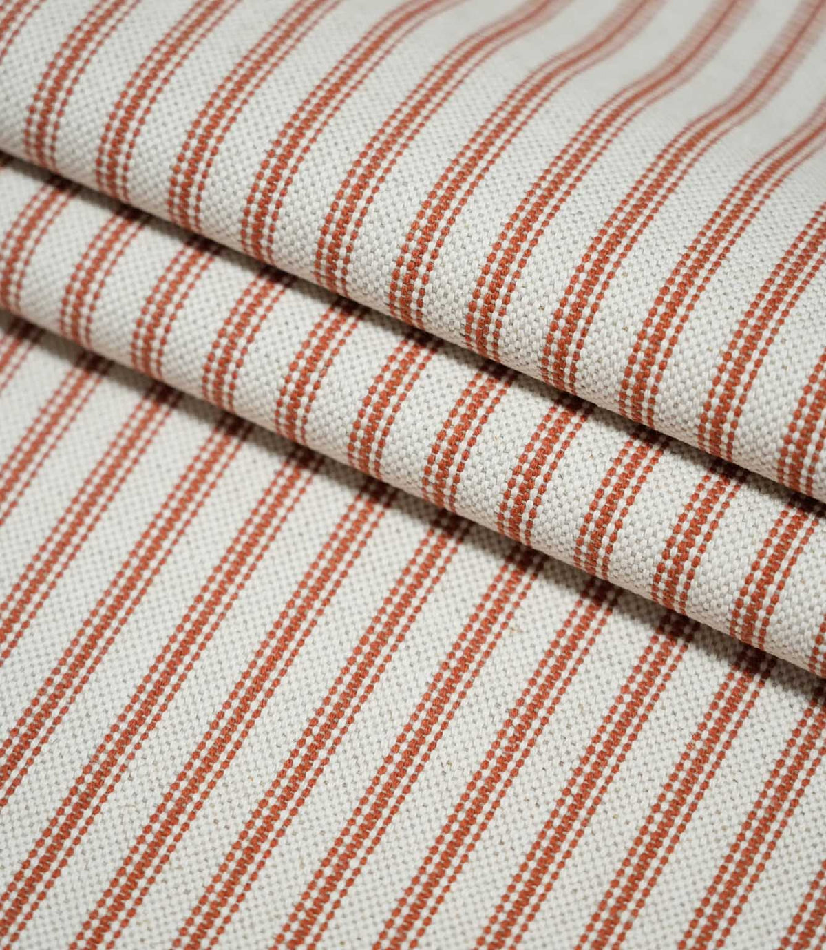Layers of folded Linen Ticking Burnt Orange fabric showcasing the narrow burnt orange stripes and textured cream woven surface.