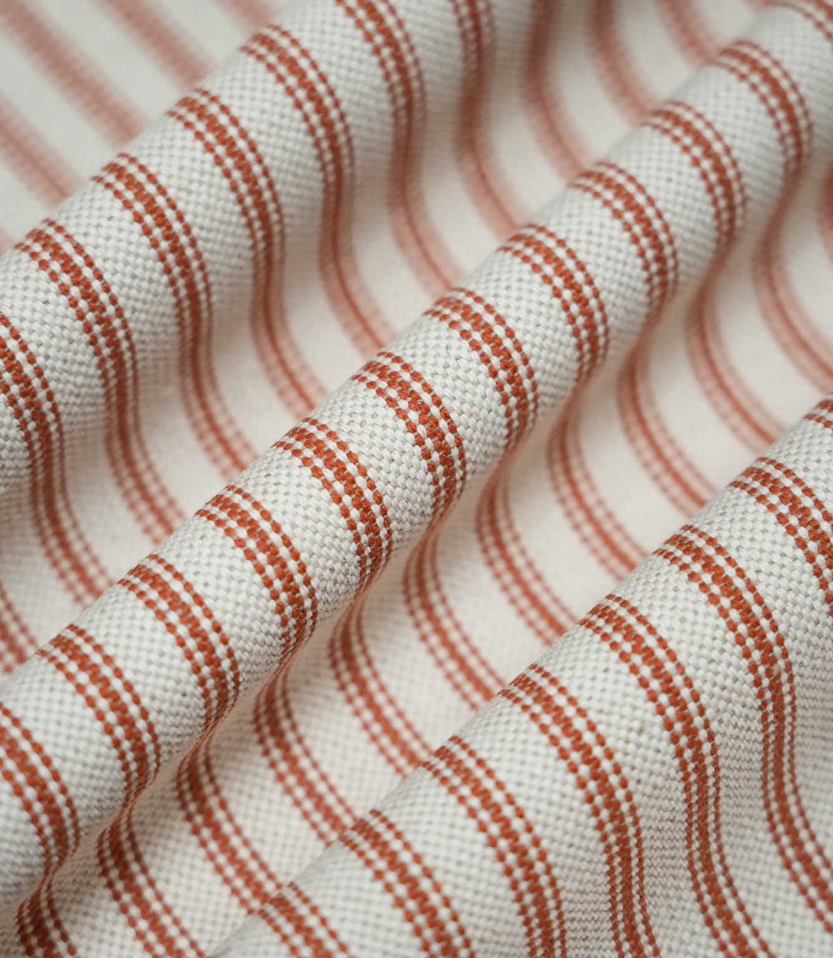Draped Linen Ticking Burnt Orange fabric with soft folds highlighting the repeating orange ticking stripes and textured woven finish.