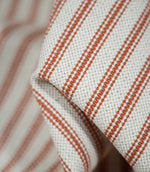 Detailed close-up of Linen Ticking Burnt Orange fabric showing the raised woven texture, fine orange stripes and natural cream background.