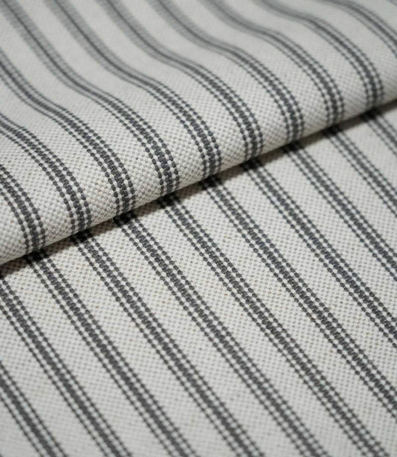 Folded grey ticking stripe fabric showing the repeating charcoal grey striped design and textured natural cream weave.
