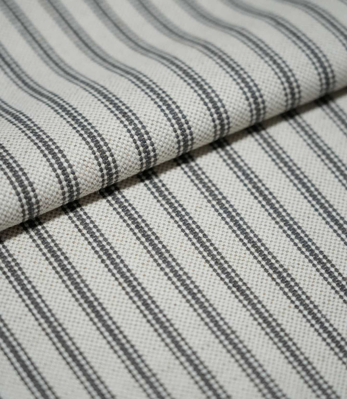 Folded grey ticking stripe fabric showing the repeating charcoal grey striped design and textured natural cream weave.