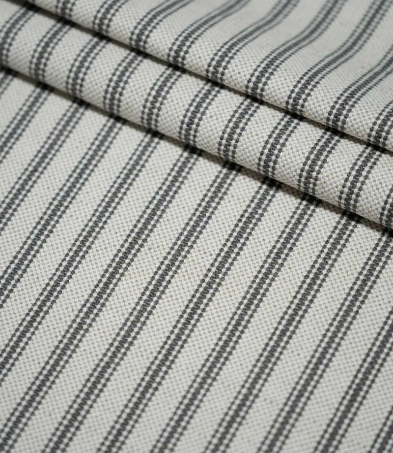 Layered folds of grey ticking stripe fabric, highlighting the evenly spaced charcoal stripes and tactile woven texture.